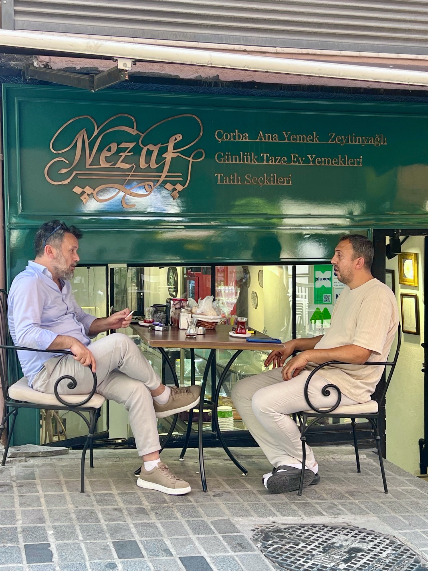 Nezaf Ev Yemekleri'nin Nişantaşı'ndaki dış cephesi; kapı önündeki masada sohbet eden iki misafir